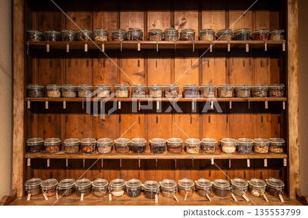 Many kind of herbal ingredients preserved inside the small vacuum glass pots on the wooden shelf. 135553799