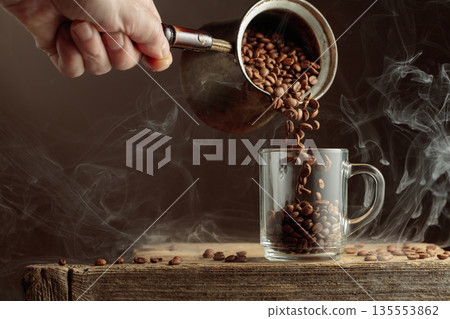 Roasted coffee beans is poured in a clear glass mug. Roasted coffee beans is poured in a clear glass mug. 135553862