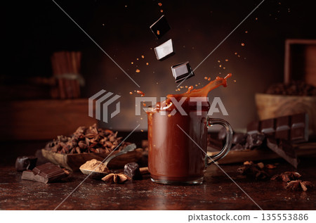 Pieces of dark chocolate fall into a glass of cocoa drink. Pieces of dark chocolate fall into a glass of cocoa drink. 135553886