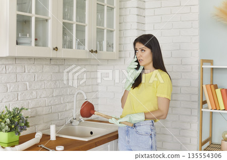 Young girl talking by the phone advising with plumber how to unclog a sink drain. 135554306