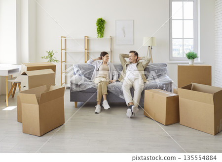 Happy couple sitting on new sofa among moving cardboard boxes and furniture Happy couple sitting on new sofa among moving cardboard boxes and furniture 135554884