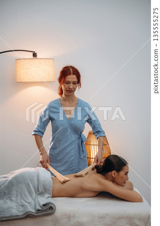Sticks in hands. Relaxed young woman getting massage by therapist in spa salon Sticks in hands. Relaxed young woman getting massage by therapist in spa salon 135555275
