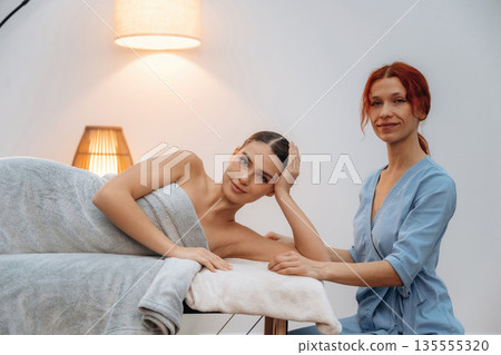 Female masseur near woman lying down in spa salon Female masseur near woman lying down in spa salon 135555320