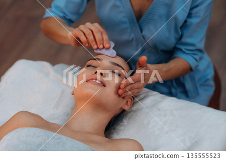 Facial massage. Relaxed young woman is with therapist in spa salon Facial massage. Relaxed young woman is with therapist in spa salon 135555523