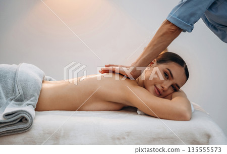 Using oil. Relaxed young woman getting massage by therapist in spa salon Using oil. Relaxed young woman getting massage by therapist in spa salon 135555573