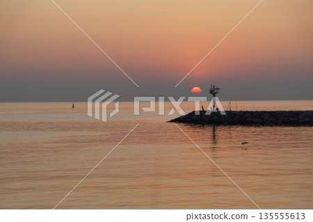 golden dawn on the sea.The dawn of a red dawn on the gray horizon of the sky, beyond a  pier.  135555613