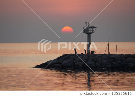 The dawn of a red dawn on the gray horizon of the sky, beyond a stone pier. The dawn of a red dawn on the gray horizon of the sky, beyond a stone pier. 135555615