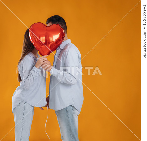 Kissing, heart shaped balloon. Lovely couple are together in the studio Kissing, heart shaped balloon. Lovely couple are together in the studio 135555941