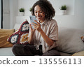 Woman With Bright Smile Reviews Playful Message On Her Smartphone Surrounded By Cozy Decor And Cushions 135556113