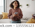 Cheerful Woman Sits On Comfortable Couch Mapping Out Travel Plans Surrounded By Natural Elements And Light 135556123