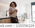 Comfortable Woman Leaning Against Kitchen Table, Laidback Lady Enjoying Coffee In Bright Apartment 135556129
