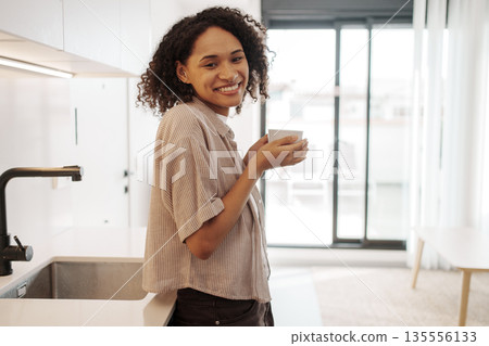 Approachable Black Woman Smiling Warmly While Holding Coffee In Contemporary Kitchen Ambiance 135556133