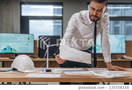 By the table with documents. Man is working in the wind turbine company 135556338