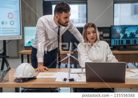 Laptop and documents on table. Two employees are working in wind turbine company Laptop and documents on table. Two employees are working in wind turbine company 135556388