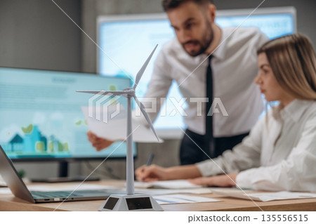 Woman is sitting, man is standing. Two employees are working in wind turbine company Woman is sitting, man is standing. Two employees are working in wind turbine company 135556515