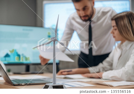 Woman is sitting, man is standing. Two employees are working in wind turbine company Woman is sitting, man is standing. Two employees are working in wind turbine company 135556516