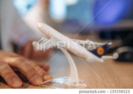 Close up focused view of toy plane on desk in airline company, man is working Close up focused view of toy plane on desk in airline company, man is working 135556523