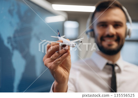 Cheerful facial expression. Man is holding toy plane, in airline company Cheerful facial expression. Man is holding toy plane, in airline company 135556525