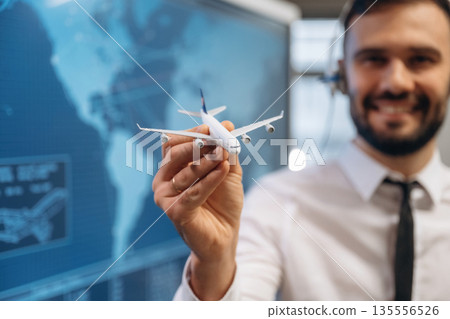 Cheerful facial expression. Man is holding toy plane, in airline company Cheerful facial expression. Man is holding toy plane, in airline company 135556526