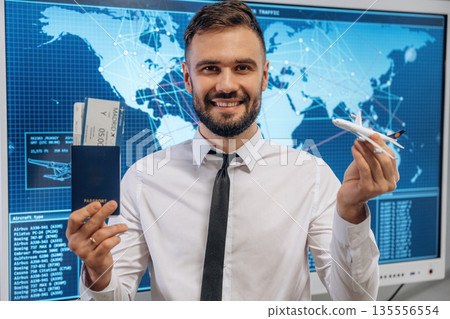 Smiling, positive facial expression. Man is holding tickets for flying indoors in airline company Smiling, positive facial expression. Man is holding tickets for flying indoors in airline company 135556554