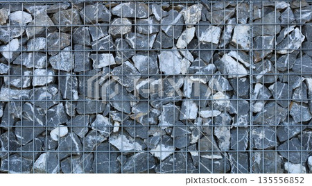 Lattice frame of landslide protection structure made of iron cage filled with rough gray natural stones, solid industrial texture graphic resource made of metal rods and rough cobblestones 135556852