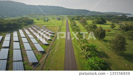 Fiji, Port Villa: solar electric panels along the road, surrounded by green fields and distant hills on Efate Island. Sustainable energy wild nature landscape. Aerial view drone flight Fiji, Port Villa: solar electric panels along the road, surrounded by green fields and distant hills on Efate Island. Sustainable energy wild nature landscape. Aerial view drone flight 135556939