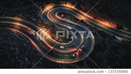 Malta: cars driving on winding night road with orange street lights, creating visually striking scene with illuminated headlights and taillights. Aerial view drone flight , top down Malta: cars driving on winding night road with orange street lights, creating visually striking scene with illuminated headlights and taillights. Aerial view drone flight , top down 135556960
