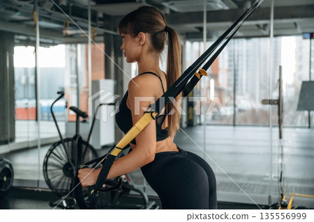 Pulls elastic ropes. Young woman is in the gym 135556999