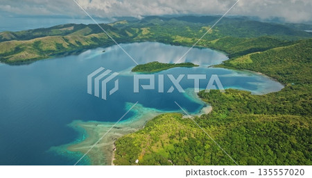Islands covered with lush green rainforests surrounding a tranquil turquoise bay, featuring shallow coral reefs reflecting clear waters and an overcast sky 135557020