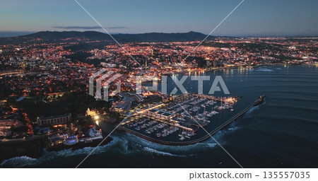 Portugal, Lisbon: Cascais glowing at dusk, aerial view of the marina and cityscape, with the Sintra mountains in the background, in Portugal. Drone Portugal, Lisbon: Cascais glowing at dusk, aerial view of the marina and cityscape, with the Sintra mountains in the background, in Portugal. Drone 135557035