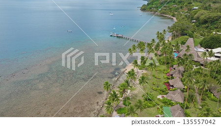 Savusavu resort with traditional bures huts and lush tropical landscape reef coastline. Exotic relaxing travel vacations and scenic views of the tranquil bay with boats and a long pier. Aerial flight 135557042
