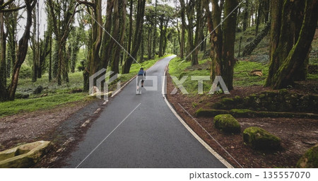 Cyclist riding bicycle on winding asphalt road through a dense, green forest in Sintra Cascais Natural Park, enjoying the tranquil outdoor environment and physical activity. Portugal, Lisbon 135557070
