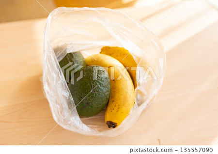 Avocado and banana on a table in a bright room - image of ripening Avocado and banana on a table in a bright room - image of ripening 135557090