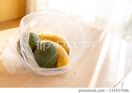 Avocado and banana on a table in a bright room - image of ripening Avocado and banana on a table in a bright room - image of ripening 135557096