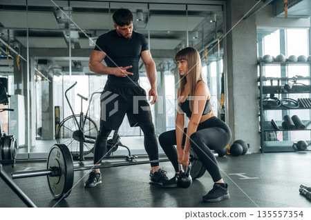 Squats with dumbbell. Man and woman are in the gym together Squats with dumbbell. Man and woman are in the gym together 135557354