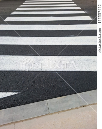 Freshly painted white lines mark a new pedestrian crossing on black asphalt. The road shows clear, sharp lines to enhance safety for walkers in the busy area. Freshly painted white lines mark a new pedestrian crossing on black asphalt. The road shows clear, sharp lines to enhance safety for walkers in the busy area. 135557422