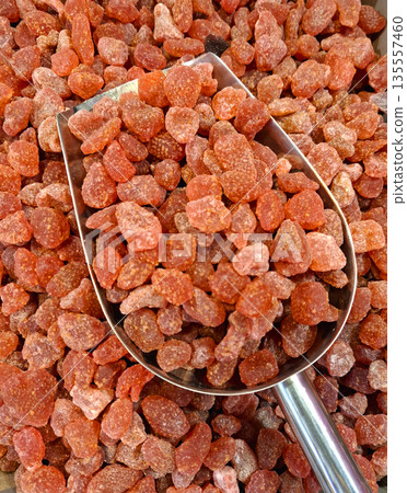 Dried strawberries are arranged in a store display for customers. Shiny scoops sit on the surface, inviting shoppers to select their preferred quantity. 135557460