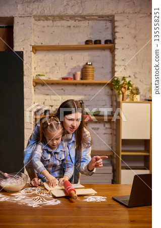 Mother explaining recipe to daughter during home baking process. Mother explaining recipe to daughter during home baking process. 135558251