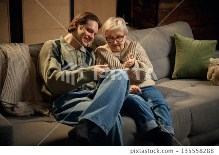 Grandmother explaining tablet content to grandson at home. 135558288
