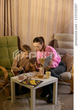 Woman and child painting together at home creative workspace. 135558307