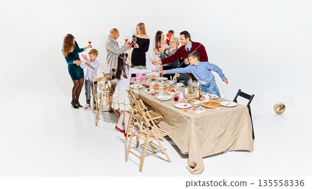 Cheerful relatives exchanging Valentine hearts around dining table. 135558336