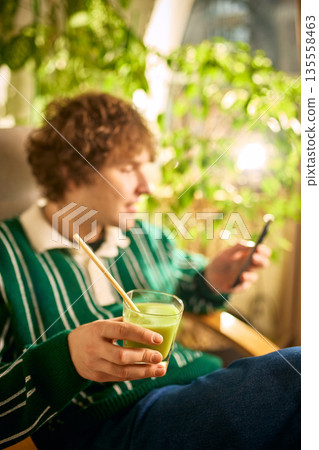 Young man holding glass of fresh juice while using smartphone. Young man holding glass of fresh juice while using smartphone. 135558463