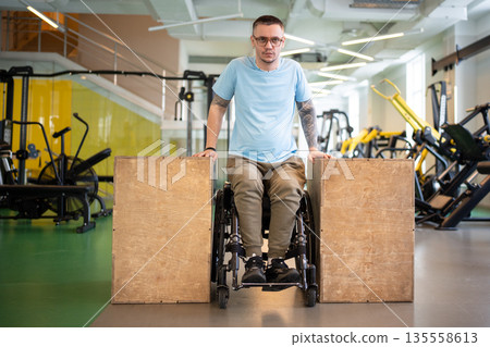 Determined disabled male in wheelchair doing upper body push ups workout using wooden blocks. 135558613