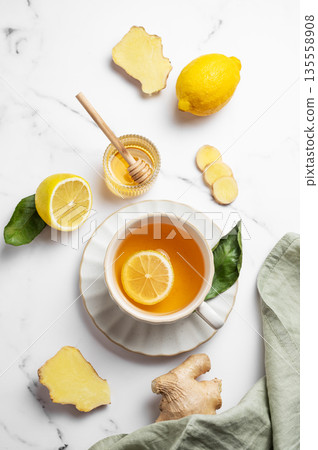 A cup of hot tea with fresh lemon and ginger on a light marble background with honey A cup of hot tea with fresh lemon and ginger on a light marble background with honey 135558908