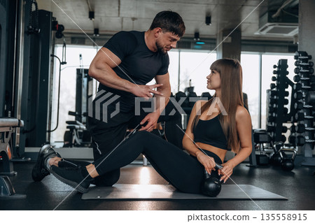 Trainer is helping. Man and woman are in the gym together Trainer is helping. Man and woman are in the gym together 135558915