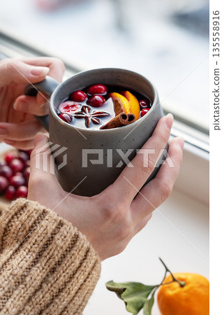 A woman holds a mug of non-alcoholic mulled wine or a spicy hot drink with orange A woman holds a mug of non-alcoholic mulled wine or a spicy hot drink with orange 135558916