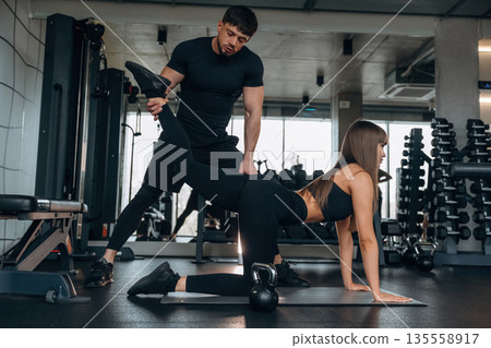 Trainer is helping. Man and woman are in the gym together 135558917