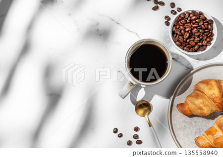 Freshly brewed black coffee in a cup on a white marble background with croissants Freshly brewed black coffee in a cup on a white marble background with croissants 135558940