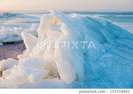 Shoreline with stacked ice slabs at sunset, winter landscape and broken crystalline layers. 135559043