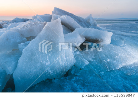 Ice slabs on a frozen coastline at sunset with evening light and deep blue shadows. 135559047